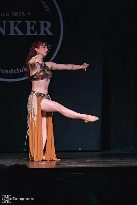 Abby im bronzefarbenen Kostüm mit hoch erhobenem Bein beim orientalischen Tanz, Imaginaerium-Show 2026
