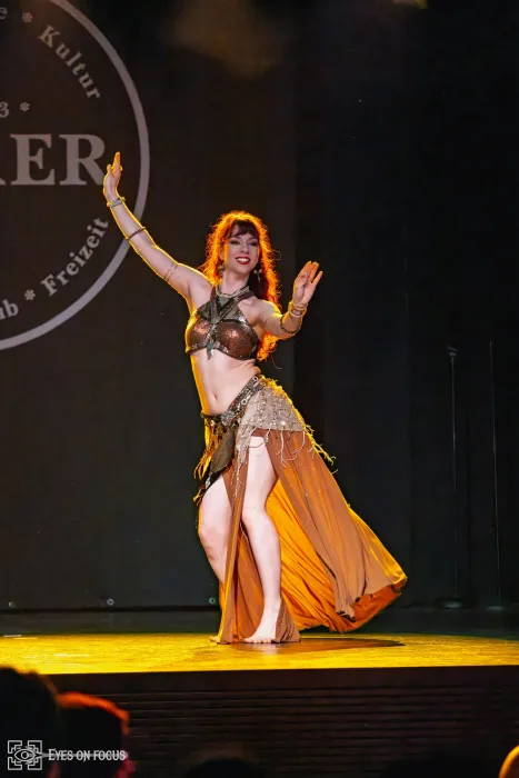 Abby lächelnd mit ausgebreiteten Armen und schwingendem Rock im goldenen Bühnenlicht